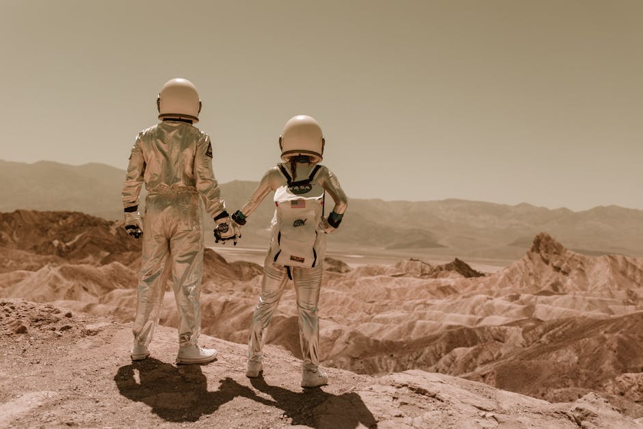 Two astronauts holding hands while exploring a desert terrain under a clear sky. Christopher Hirata - Nasa