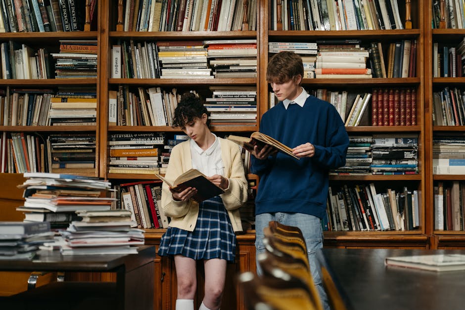 Two students reading in a library, surrounded by bookshelves filled with literature.